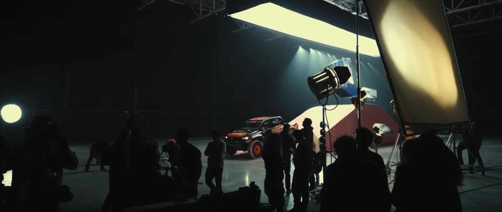 Coche de rally iluminado en un plató, con el equipo de rodaje de Glassy Films a contraluz